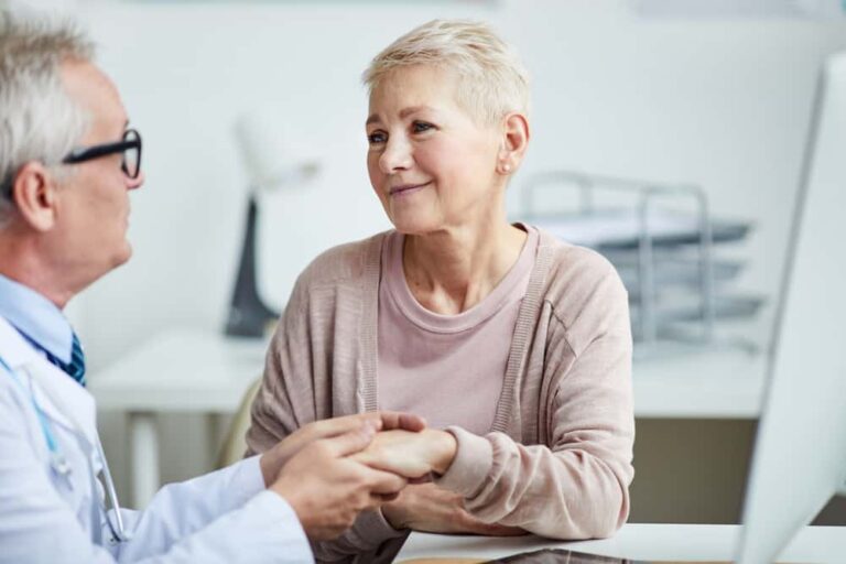 A senior woman consulting with a doctor in an office, sharing a compassionate moment during a medical discussion.