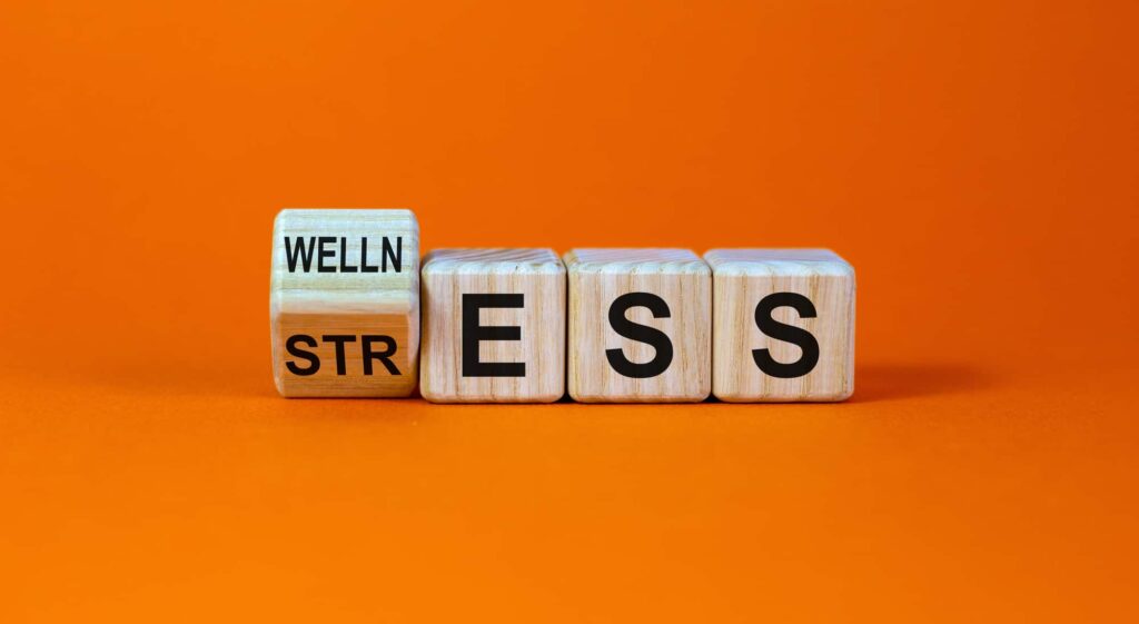 Wooden blocks showing the transition from "stress" to "wellness" on an orange background, representing the shift toward a healthier lifestyle.