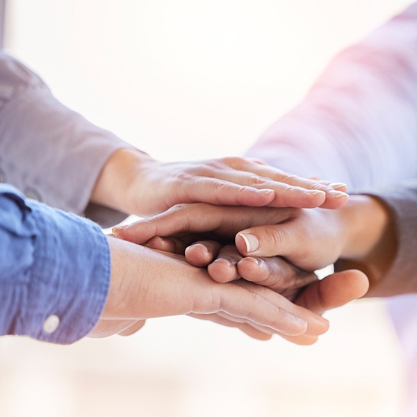 A close-up of multiple hands stacked together, symbolizing teamwork, support, and unity in mental health care.