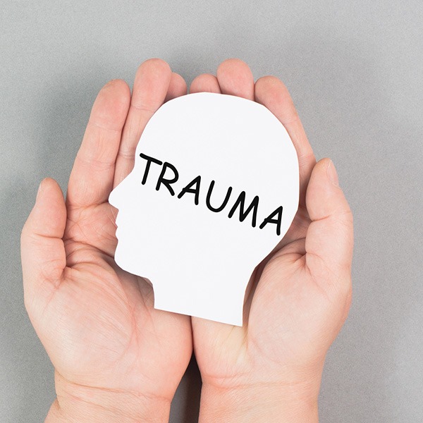Hands gently holding a paper cutout of a human head with the word "TRAUMA" written on it, symbolizing mental health awareness and recovery support.